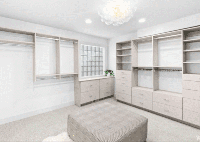 Spacious walk-in closet with built-in shelves, drawers, hanging rods, a window, and a large plaid ottoman in the center.